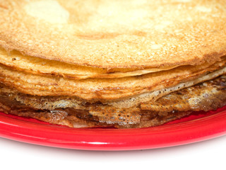 Staple of wheat golden yeast pancakes or crepes on red plate on a white background closeup