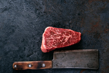 Raw marbled steak from the shoulder blade beef with a meat cleaver on a dark background