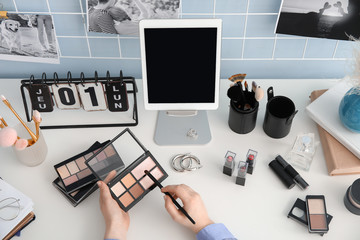 Makeup artist at table with modern tablet computer and cosmetics