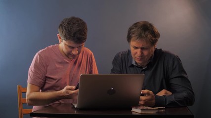 concentrated young man with phone shows how to input data to senior father at table in room slow motion. Concept technology education - Powered by Adobe