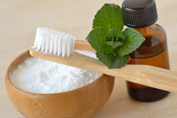 Baking soda in a bowl with a wooden toothbrush and peppermint essential oil - Homemade natural...