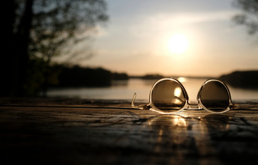 Fototapeta na wymiar A calm sunset at a lake with a pair of sunglasses in the foreground