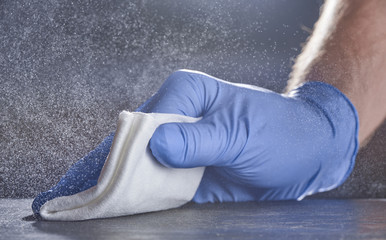 A hand in a medical glove wipes the table. Grey background with splashes of disinfectant.