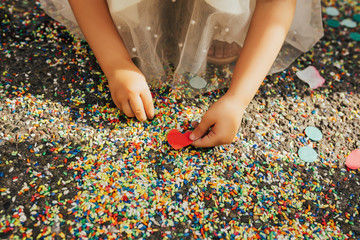 Close up of multi-colored rice cover the ground  after a wedding ceremony. Hands of girl hold red heart.