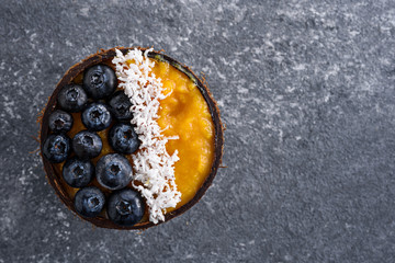 top view smoothie dessert of frozen mango, blueberry and coconut puree in coconut bowl on dark background