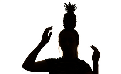 Pineapple in a woman's hands above the head - silhouette on white background, girl having fun when trains balance with exotic fruit