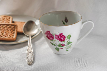 Vintage porcelain cup with spoon and saucer with cookies on a white background in Ukraine. Morning light. Copy space.