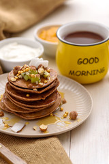 vertical vegetarian chocolate pancakes with kiwi, nuts and honey with sour cream, mango jam and yellow cup of cocoa on white background