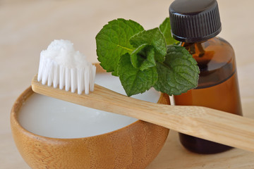 Coconut oil in a bowl with a wooden toothbrush and peppermint essential oil - Homemade natural toothpaste