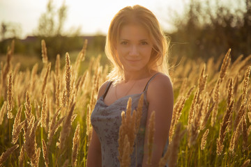 young girl with blond hair in a light sundress stands in the sun