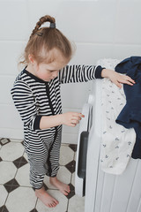 Cute girl in striped clothes turns on the washing machine. Cleanliness and Household Concept