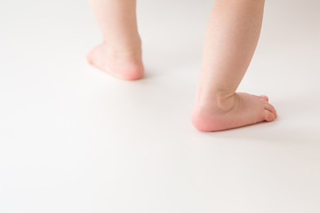 Infant legs on light gray floor background. Baby first steps. Closeup. Back view.