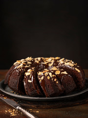 Chocolate bundt cake with chocolate glaze and almonds and cut slices on a dark background with copy space.