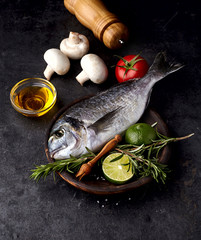 Dorado fish in the wooden plate  on black background with lime, rosemary, tomato  and mushrooms.
