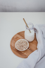 Non dairy alternative vegan oat milk in bottle with bamboo eco zero waste straw and fresh oats on wooden tray. Gluten and lactose free products.