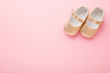 Golden baby shoes on light pink floor background. Pastel color. Closeup. Empty place for text. Top down view.