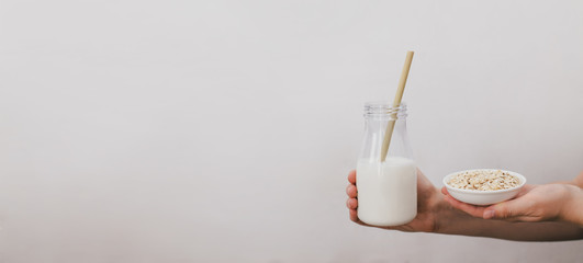 Non dairy alternative vegan oat milk in bottle with bamboo eco zero waste straw and fresh oats in woman hands. Gluten and lactose free products.