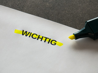 Sheet of paper on a desk showing the word WICHTIG (German for IMPORTANT). Text highlighted in...