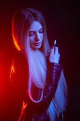 Fashion portrait of beauty model woman in bright lights smoking e-cigarette. tobacco heating system