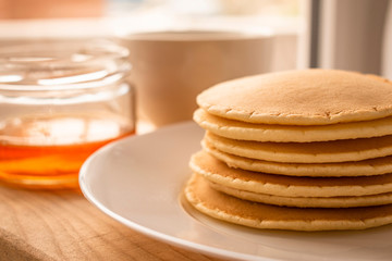 Fototapeta na wymiar Pancake lying on a white plate behind the glass jar with honey and a mug of tea 
