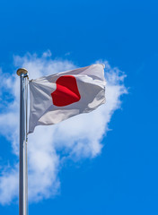 Japanese National Flag waving in the wind against a sunny blue sky.