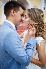 Naklejka premium Young stylish guy in the costume of the groom and the bride beautiful girl in a white dress with a train walking on the background of a large house with columns on their wedding day