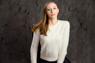 Studio portrait of a pretty happy blonde girl. Model posing on a chair on a gray stylish background.