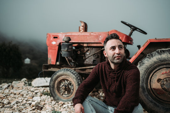 Armenian Caucasian man sits on the old broken red tractor in the mountains during the foggy day. Finding the interesting abandoned things while travelling. Travel concept. Natural skin tone - Powered by Adobe