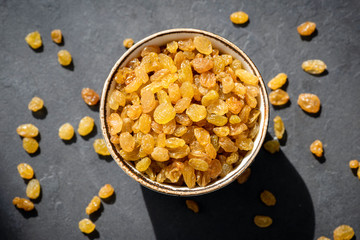 Golden raisins or sultana in bowl on black background, table top view. Dried fruit, healthy snack food