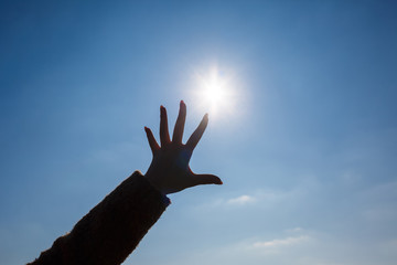 silhouetted a female hand against a blue sky and bright sun