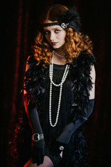 Portrait of old-fashioned red haired woman dressed in style of Great Gatsby era shows her legs and...