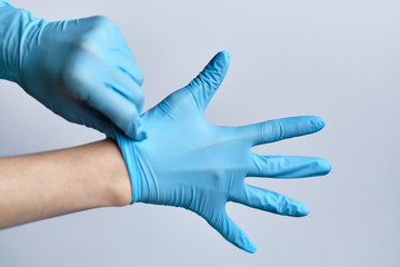 The process of putting blue medical gloves on hands on a white background.