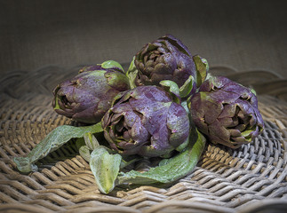 fresh artichokes in circular composition - rustic straw background - violet artichoke of sant...