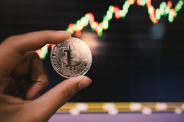 Bitcoins is virtual money. Gold bitcoins on hand  with chart of growing and falling valuance of a cryptocurrency. Mining or blockchain technology.