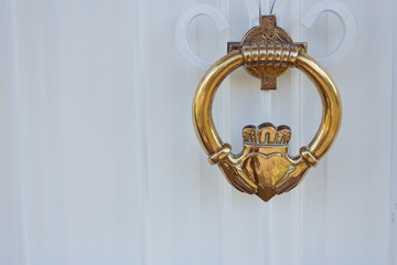 Brass knocker with Irish Claddagh design on white painted door.  Irish travel concept.