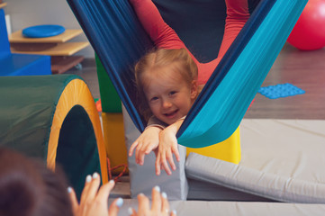 girl enjoying a sensory therapy on a hammock while physiotherapist assisting her - obrazy, fototapety, plakaty