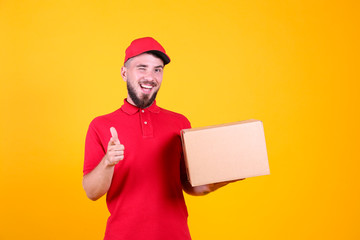 Young handsome delivery guy wearing red uniform and cap holding the blank cardboard box over...