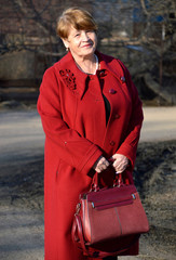 Portrait of stylish 67 year old woman in a bright red coat with a burgundy bag kindly and sincerely...