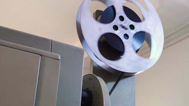 CU: light grey spool with black reel rotates on vintage cinema equipment to show retro movie in room close low angle shot