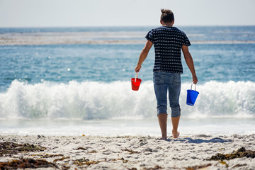 Mann holt Wasser für eine Sandburg am Strand mit blauem und rotem Eimerchen