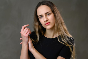 Naklejka premium Horizontal portrait of a caucasian girl in a black dress with long hair on a gray background.