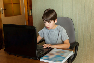 A ten-year-old schoolboy learns at home using a laptop. The concept of distance education in connection with the coronavirus pandemic