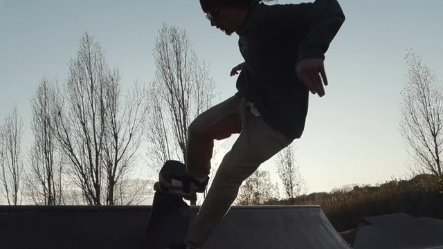 Skater does big air out of a quarter pipe  and grabs the board on a beautiful sunset session. Rides a streetboard, a cross between skateboard and snowboard