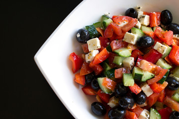 fresh greek salad in white plate on black table. vegetable salad with feta cheese. healthy food.