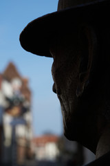 Shilouette of the head of a sculpture against a blurred background with the view of buildings of a city