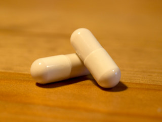 two white pills capsules close up macro on wooden background. antibiotics