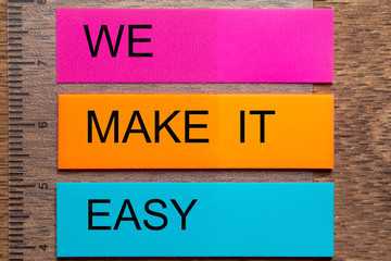 Three bookmark stickers with the words WE MAKE IT EASY, on a dark natural wooden table