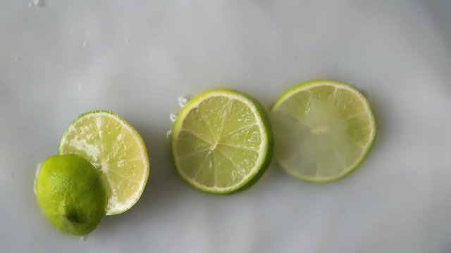 Sliced limes falling in milky water. White liquid splashing around fresh green fruits.