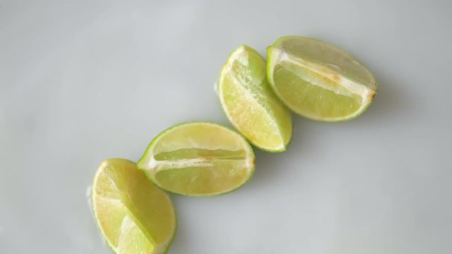 Green Lemons, citrus aurantifolia fruits falling on water in slow motion. splashes on white background.