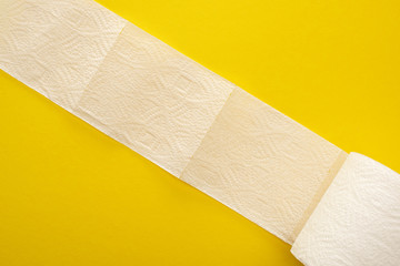 top view of unrolled white toilet paper on yellow background